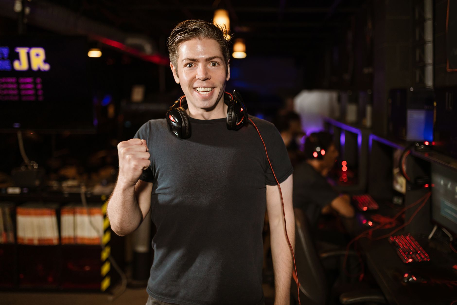 Smiling man with headphones and fist raised, celebrating in a gaming arena