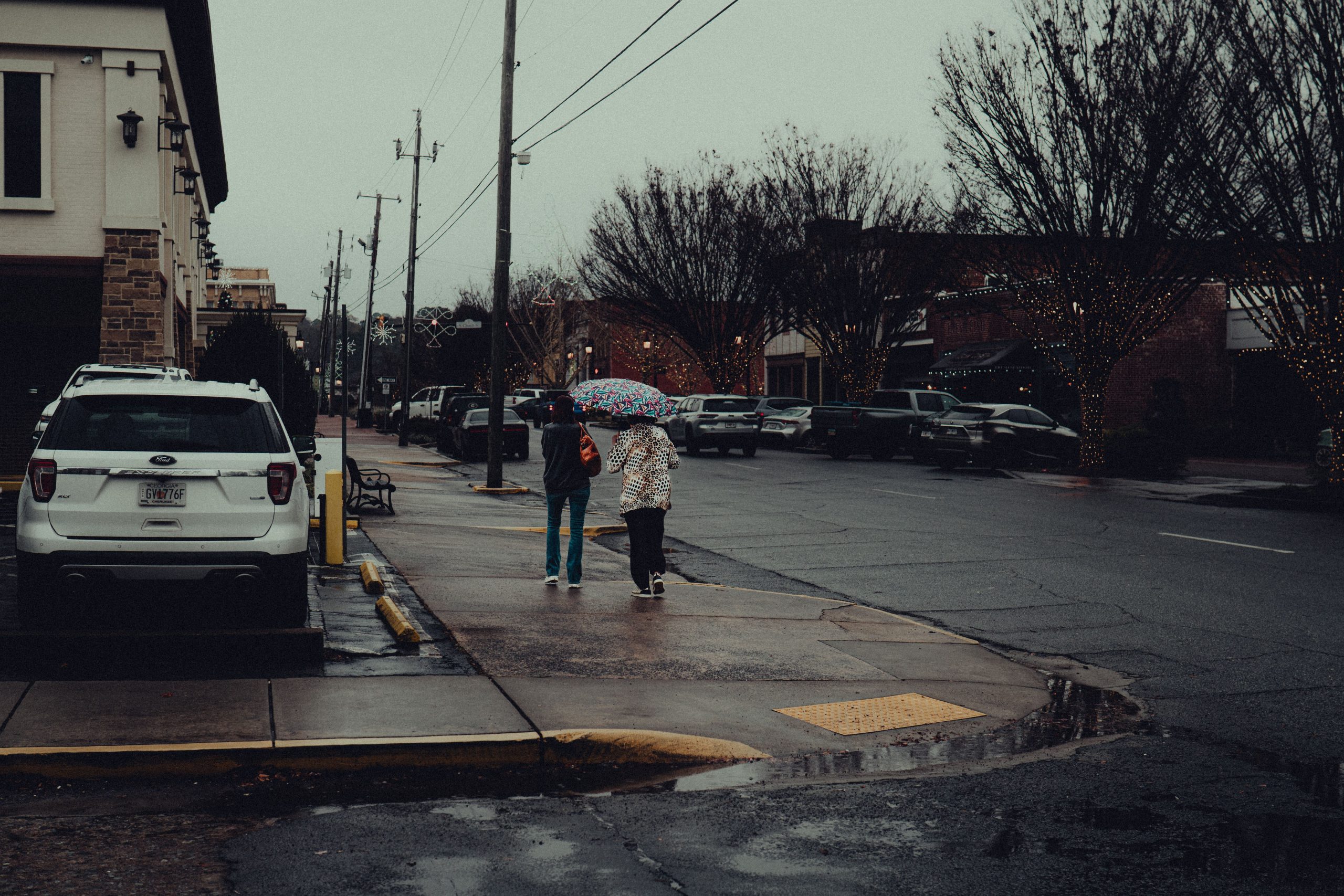 A moody, rainy street scene in downtown Canton, Georgia, featuring pedestrians with umbrellas