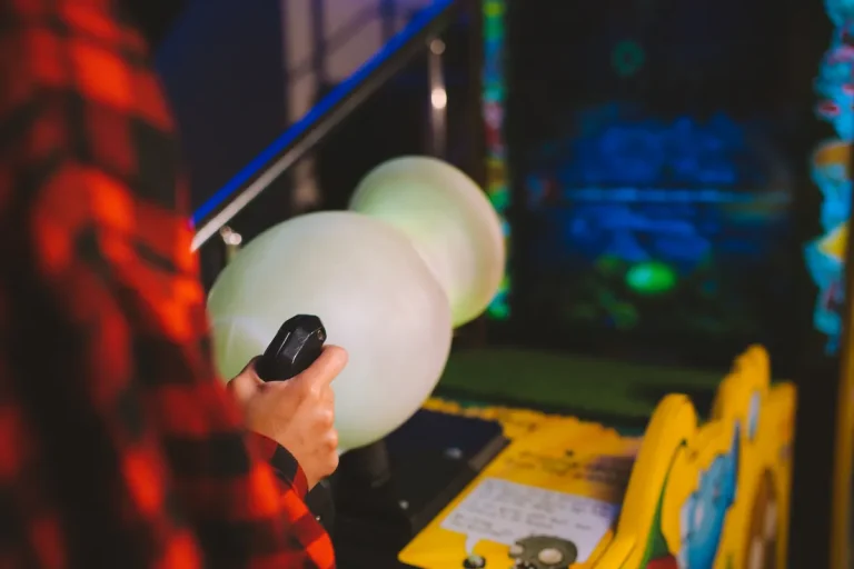 Close-up of a person playing an arcade machine with vibrant lights in a gaming arcade
