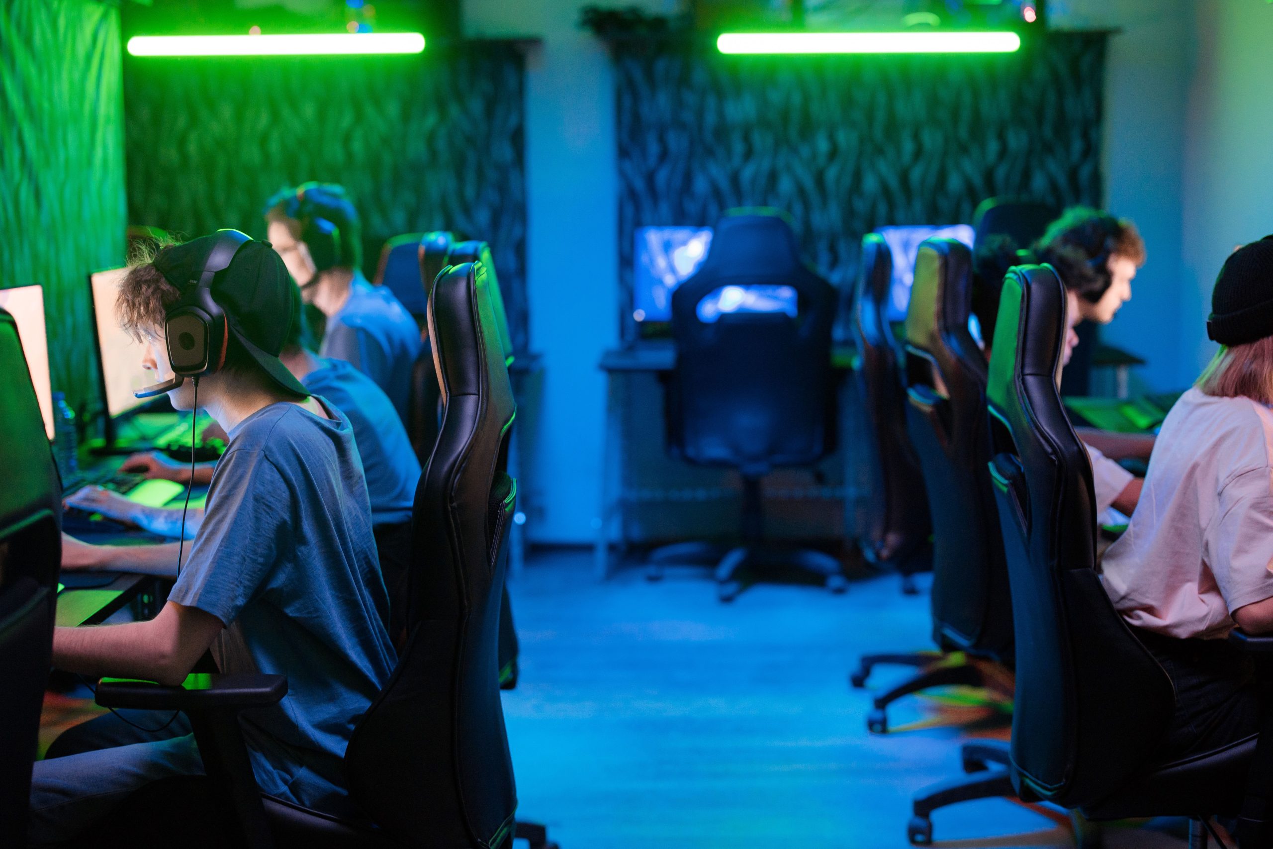Gamers wearing headsets sit at computers under green and blue lights