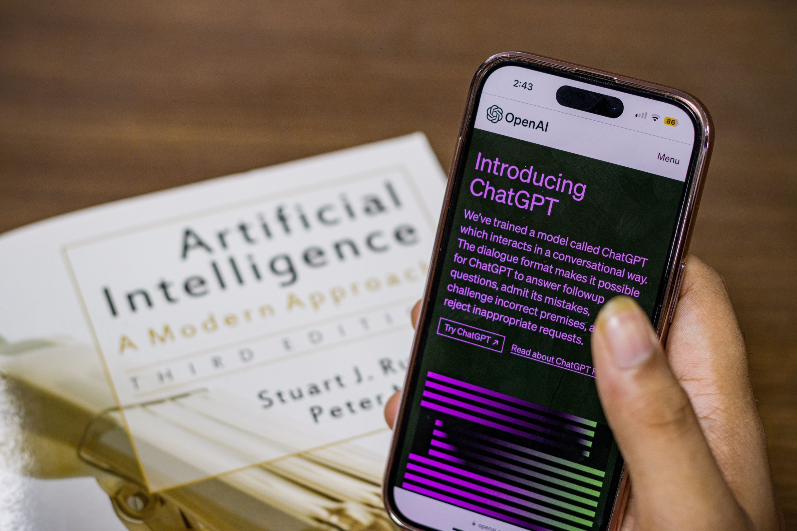 Close-up of a smartphone displaying ChatGPT app held over AI textbook