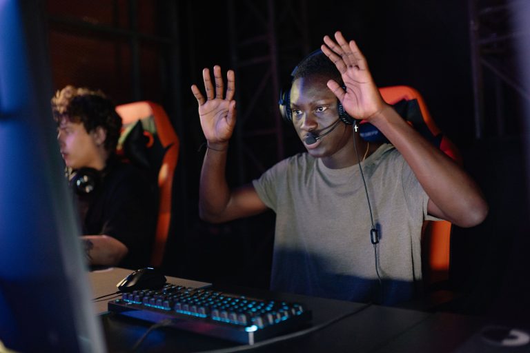 A gamer wearing a headset raises both hands at a computer