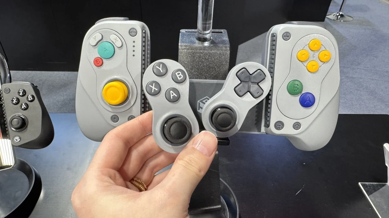 A hand holds a compact game controller beside several controller designs